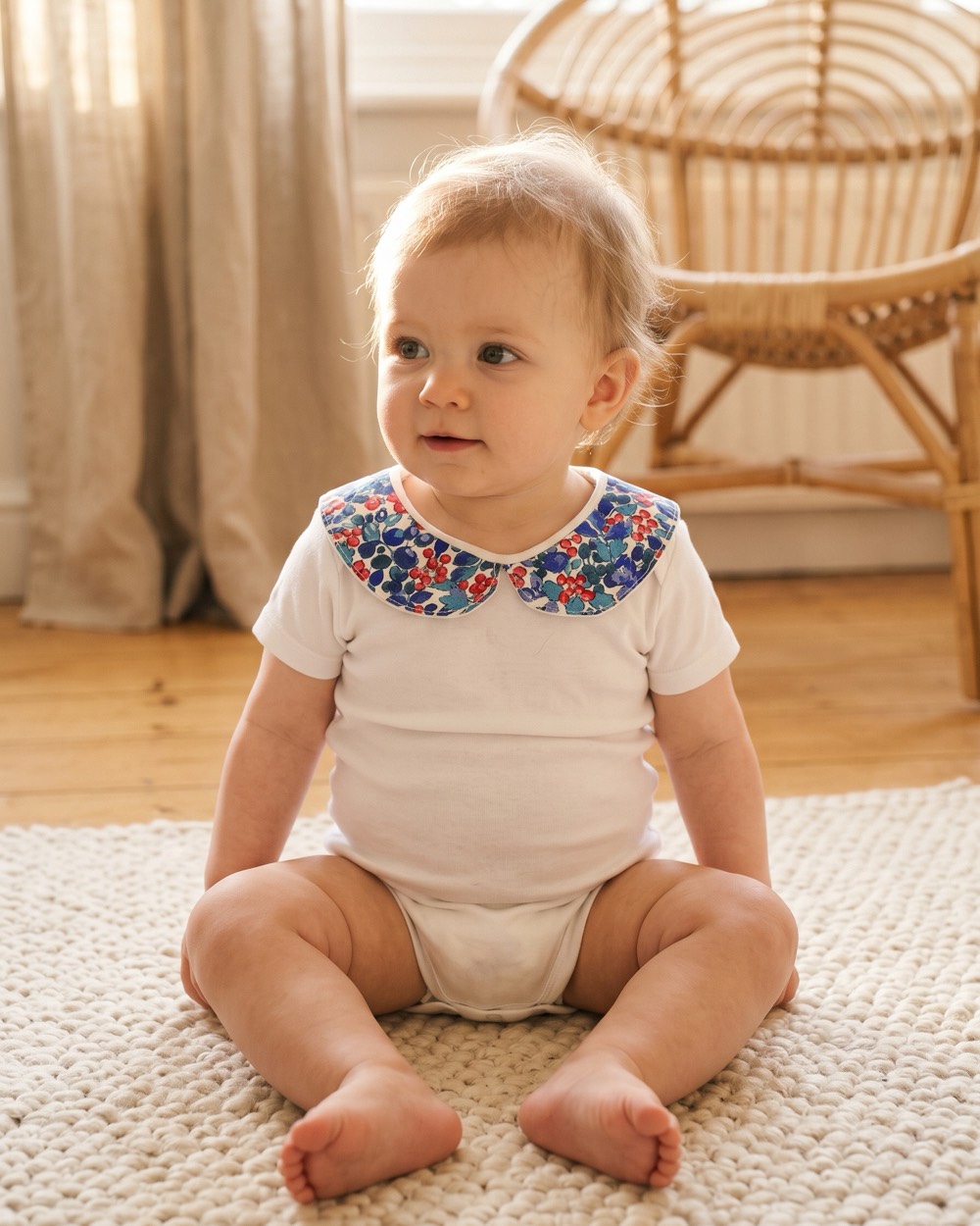 Bébé assis portant le body blanc à col Claudine fleuri bleu