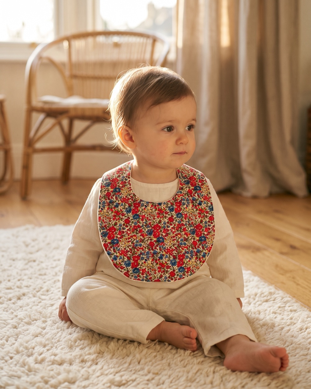 Bébé assis sur un tapis, portant un bavoir Calou en Liberty fleuri rouge et bleu