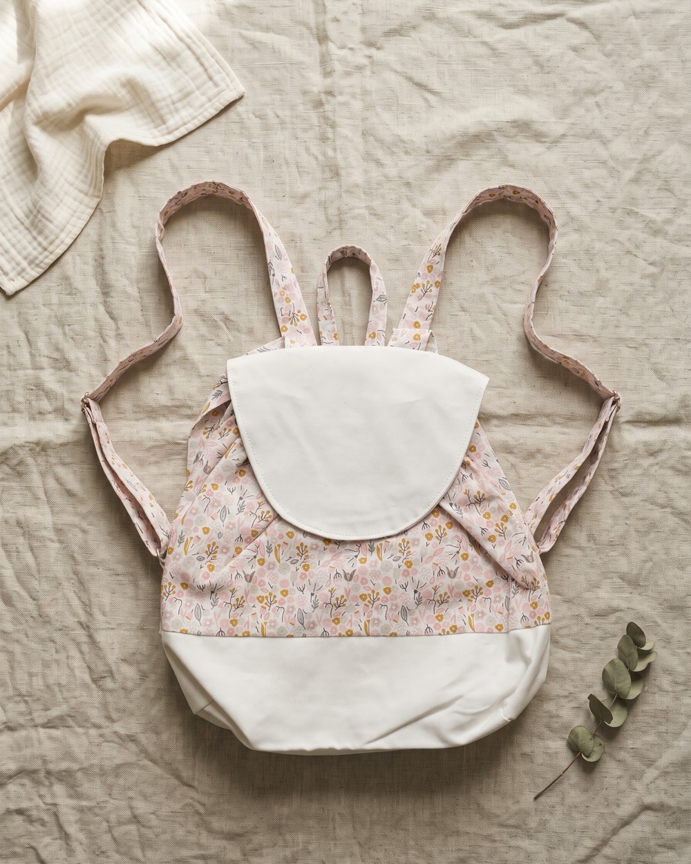 Sac à dos enfant posé à plat sur du lin écru, bretelles déployées
